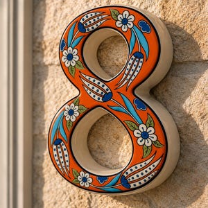 May include: A ceramic house number eight featuring a vibrant orange background decorated with hand-painted blue and white floral patterns, including stylized tulips and small blossoms with green leaves, finished with a glossy, smooth surface.