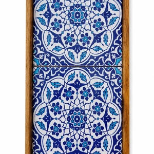 May include: A rectangular wooden serving tray featuring two inset ceramic tiles. The tiles display a symmetrical floral pattern in shades of deep blue, light blue, and white. The tray has integrated handles on the top and bottom edges.