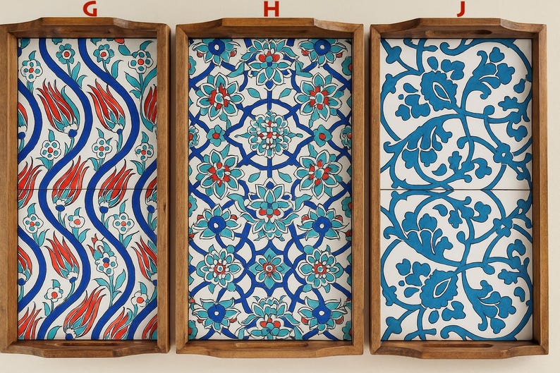 May include: Three rectangular wooden serving trays labeled G, H, and J. Each tray features a distinct ceramic tile inlay with intricate floral patterns in shades of blue, red, and white. The trays have raised edges and integrated handles.