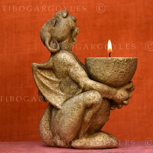 Puede incluir: Un candelabro de gárgola color piedra con una vela encendida. La gárgola está arrodillada y sostiene un candelabro en forma de cuenco. El fondo es de color naranja liso. El texto "TIBOGARGOYLES" es visible.
