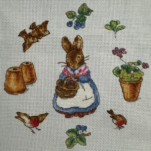 May include: A brown rabbit with a blue and white dress and a brown basket is surrounded by birds, flowers, and pots. The rabbit is holding the basket in its paws.