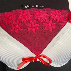 May include: A white bra with vertical stripes and red bows. The centre panel is a deep red with embroidered bright red flowers. The text "Bright red flower" is at the top.