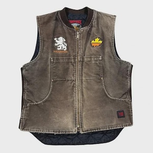 May include: Brown work vest with a full-length zip, two front pockets, and a black quilted lining. Features a white lion patch and a yellow and orange patch. The vest has the text "DUTCHBROTHERS" and "TOUGH DUCK".