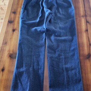 May include: Dark blue denim pants with a high waist and a straight leg. The pants have a classic five-pocket design and a Wrangler logo on the back pocket. The pants are made of a sturdy denim material.