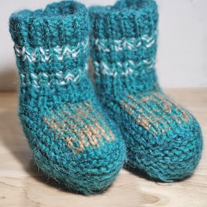 Könnte beinhalten: Ein Paar tealblaue gestrickte Hausschuhe mit weißen und braunen Akzenten. Die Socken sind aus einem weichen, flauschigen Garn gefertigt.