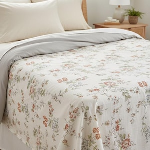 May include: A bed featuring a floral patterned duvet cover and a grey top sheet. The duvet cover has a cream background with red, green, and grey floral designs. Two cream-coloured pillows rest on the bed, with a wooden headboard.
