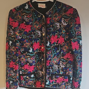 Peut inclure: Veste matelassée noire avec un motif floral vibrant dans les tons de rose, rouge, bleu et vert. La veste a un col rond, une bordure dorée et deux poches avant. L'étiquette indique "Danport's".