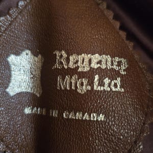 May include: Close-up of a brown leather tag with the text "Regency Mfg. Ltd." and "MADE IN CANADA" in gold lettering. The tag has a decorative, scalloped edge and a leather symbol.