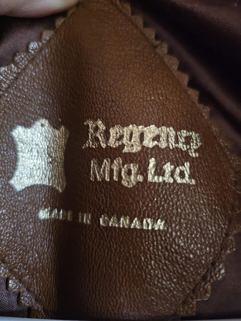 May include: Close-up of a brown leather tag with the text "Regency Mfg. Ltd." and "MADE IN CANADA" in gold lettering. The tag has a decorative, scalloped edge and a leather symbol.