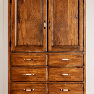 May include: A tall, wooden cabinet with a warm, brown finish. The cabinet has two upper doors and six drawers. The doors and drawers have white and gold hardware. The cabinet has curved legs.