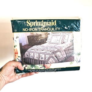 May include: A packaged Springmaid flat sheet set. The packaging is green and white with the words "Springmaid" and "NO-IRON TRANQUILITY". The sheet set features a floral pattern with a gray border. The flat sheet is for a 198 x 203 cm mattress.
