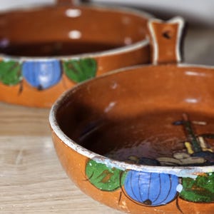 Peut inclure: Deux bols en céramique brune avec des motifs floraux peints. Les bols ont des anses et sont décorés de peinture bleue, verte et jaune.