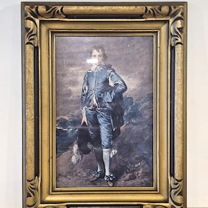 May include: A framed print of a portrait of a young person in a blue suit, holding a hat. The portrait is set against a cloudy, dark background. The frame is ornate, with a gold finish and dark brown accents.