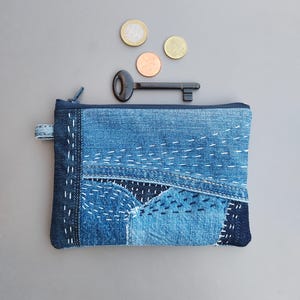May include: A rectangular denim zip-up pouch featuring patchwork construction with visible white sashiko-style stitching. The pouch is accompanied by a dark metal skeleton key and three assorted coins, including a copper-coloured and two gold-coloured coins.