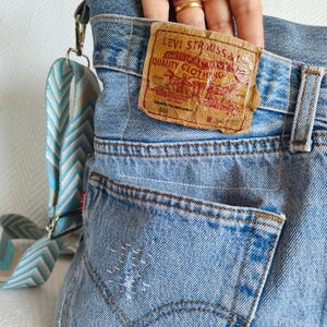 under the tag of the repurposed faded blue jeans there is a small pocket, the fingers of the model hand are half way inside the pocket.
The tag is in brown card color with printed red letters and design.