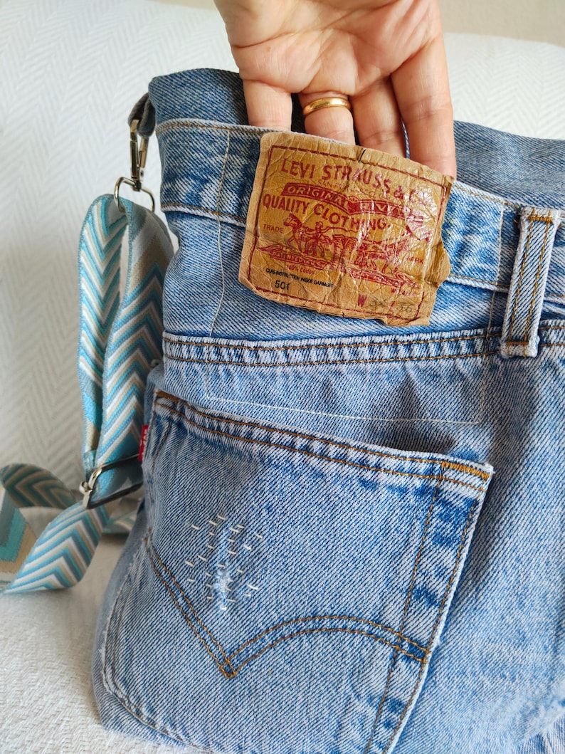under the tag of the repurposed faded blue jeans there is a small pocket, the fingers of the model hand are half way inside the pocket.
The tag is in brown card color with printed red letters and design.