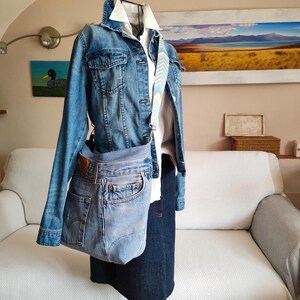 a light blue upcycled jeans bag worn across a black iron mannequin.
The mannequin has a denim jacket and a dark blue skirt on.