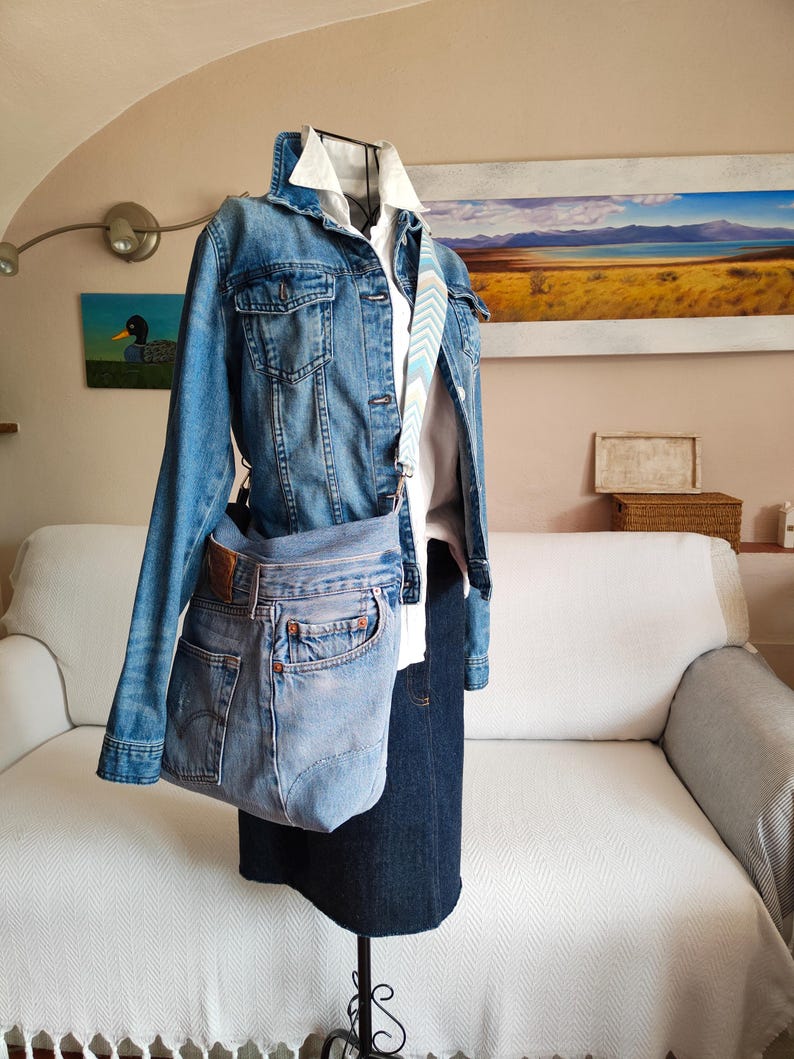 a light blue upcycled jeans bag worn across a black iron mannequin.
The mannequin has a denim jacket and a dark blue skirt on.