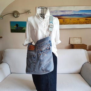 a upcycled denim crossbody bag on a black iron mannequin wearing a white shirt and a dark blue denim skirt.
The faded blue jeans bag is worn cross the body with its jacquard adjustable strap.