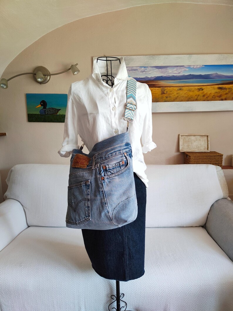 a upcycled denim crossbody bag on a black iron mannequin wearing a white shirt and a dark blue denim skirt.
The faded blue jeans bag is worn cross the body with its jacquard adjustable strap.