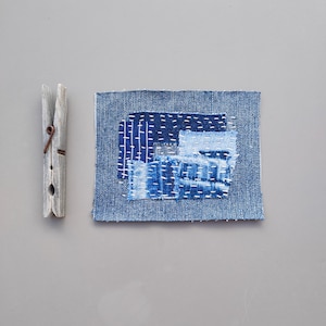 May include: A small square piece of fabric made from blue denim with different shades of blue denim sewn together in a patchwork design.