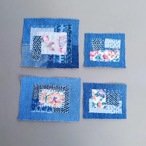 May include: Four small, rectangular fabric patches. Each patch is framed with blue denim and features a central design of floral or geometric patterns in shades of blue, white, and pink. The patches are arranged on a grey surface.