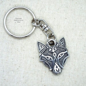 May include: Silver wolf head keyring with intricate details and a silver ring. The wolf's eyes are black and the keyring has a silver split ring.