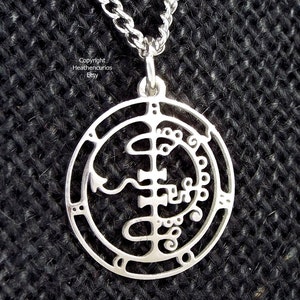 May include: Silver pendant necklace featuring a circular design with intricate details. The pendant is a sigil, a symbol used in magic and witchcraft.