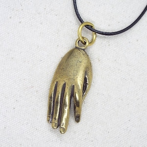 May include: A gold-toned pendant necklace featuring a detailed hand charm. The hand is open with fingers extended and appears to be made of metal.