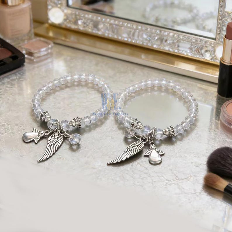 Puede incluir: Dos pulseras el&aacute;sticas hechas de cuentas transparentes facetadas con detalles en metal plateado. Cada pulsera presenta dos dijes colgantes: uno con forma de ala de &aacute;ngel y otro con forma de figura de &aacute;ngel estilizada, ambos en acabado plateado.