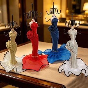 May include: Four jewelry display stands shaped like mannequins wearing floor-length gowns in gold, red, blue, and silver. Each stand features a black metal wire rack with multiple hooks for hanging necklaces and bracelets, topped with a decorative flower.