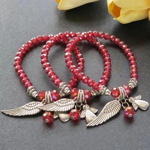 Puede incluir: Tres pulseras el&aacute;sticas hechas de cuentas rojas facetadas. Cada pulsera presenta dijes de metal en tono plateado, que incluyen alas de &aacute;ngel detalladas y peque&ntilde;as figuras de &aacute;ngeles. Las cuentas son uniformes en tama&ntilde;o y color en las tres piezas.