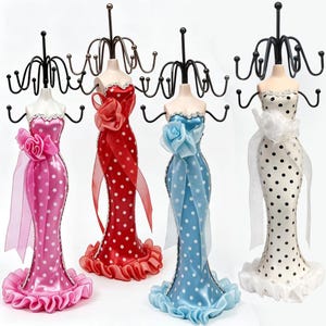 May include: Four jewelry display stands shaped like mannequins wearing strapless gowns with polka dot patterns in pink, red, blue, and white. Each mannequin features a black metal wire rack at the top for hanging necklaces and bracelets.