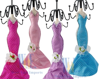 May include: Four decorative jewelry stands shaped like dresses. Each dress is a different color: fuchsia, pink, purple, and blue. The dresses have white polka dots and are adorned with lace and floral accents. Each stand has a black metal top with hooks.