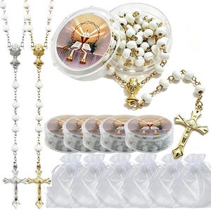 May include: White beaded rosaries with gold and silver crucifixes and chalice accents. The image includes rosaries in clear plastic containers with religious imagery, small white drawstring bags, and a close-up of a rosary.