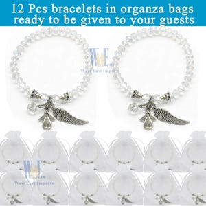 Puede incluir: Doce pulseras con cuentas facetadas transparentes, un dije de &aacute;ngel plateado y un dije de ala plateado. Cada pulsera est&aacute; empaquetada individualmente en una bolsa de organza blanca. El texto 12 Pcs bracelets in organza bags ready to be given to your guests es visible en la parte superior.