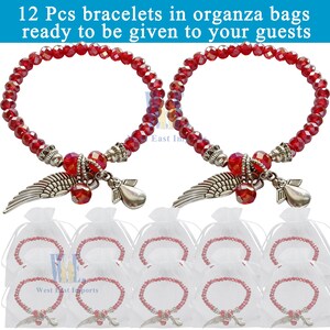 Puede incluir: Doce pulseras de cuentas rojas facetadas con dijes de alas de &aacute;ngel y &aacute;ngeles en tono plateado. Cada pulsera est&aacute; empaquetada individualmente en una peque&ntilde;a bolsa de organza blanca transparente. El texto 12 Pcs bracelets in organza bags ready to be given to your guests es visible.