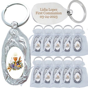 May include: Silver-toned keychains with religious imagery, including a chalice, flowers, and the letters IHS. One keychain has the text "Lidia Lopez First Communion 03-24-2023". Several keychains are packaged in white organza bags.