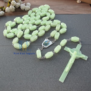 May include: A green glow-in-the-dark rosary with a silver crucifix and a silver pendant featuring a religious image. The rosary beads are faceted and have a slightly translucent appearance.