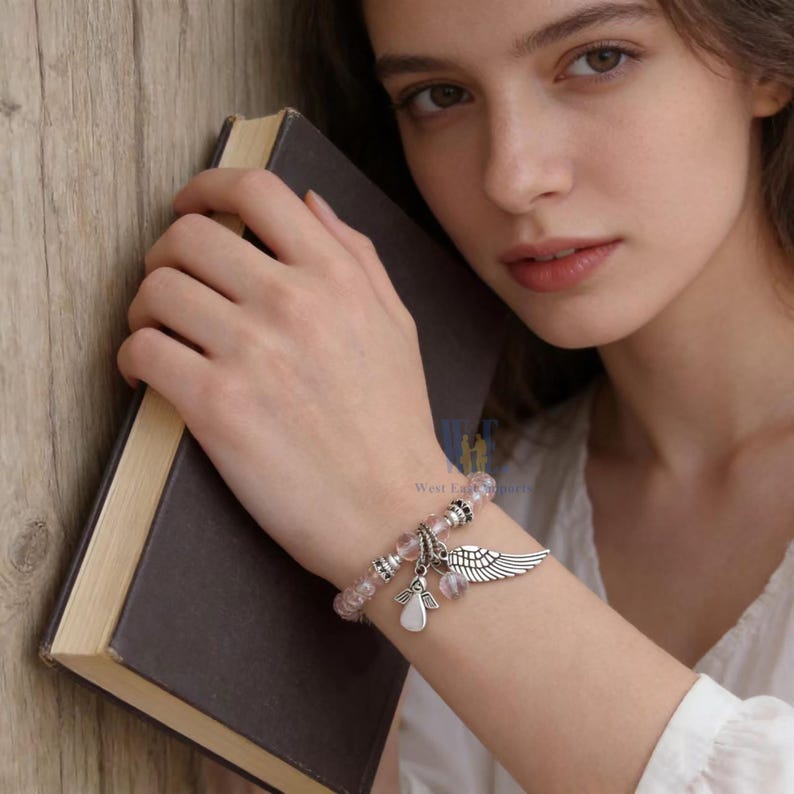 Puede incluir: Una pulsera de cuentas con cuentas esf&eacute;ricas de color rosa claro transl&uacute;cido, espaciadores de tono plateado y dos dijes de metal colgantes. Un dije tiene forma de figura de &aacute;ngel estilizada y el otro tiene forma de ala emplumada.