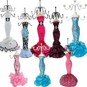 May include: A collection of eight mannequin-style jewelry stands shaped like figures in various evening gowns. Each stand features a metal wire rack at the top for hanging accessories, with dresses in colors including white, pink, blue, and purple.