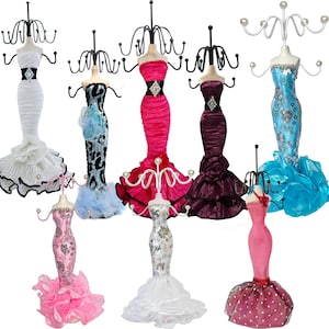 May include: A collection of eight mannequin-style jewelry stands shaped like figures in evening gowns. Each stand features a metal wire top for hanging necklaces and bracelets, with dresses in various colors including white, pink, blue, and purple.