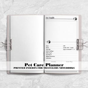 May include: An open pet care planner notebook with white pages held by two silver metal binder clips. The right page features a Pet Profile section with fields for name, breed, DOB, gender, coat color, markings, tag number, microchip ID, and allergies.
