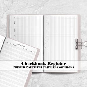 May include: Two open checkbook register booklets with white pages featuring grey grid lines and columns labelled Date, Transaction, Amount, and Balance. A silver metal binder clip is attached to the right edge of the open booklet.