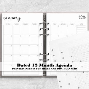 May include: A light pink ring-bound planner open to a January 2026 monthly calendar page with black text and grid lines. The planner includes additional loose white paper inserts featuring dot grid, graph, and lined layouts for organization.