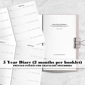 May include: A 5-year diary set consisting of printed paper inserts for travelers notebooks. The white pages feature black text, including dates like January 1st and March 2nd, with lined and grid layouts. A metal binder clip holds the booklets together.
