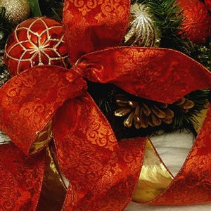 Könnte beinhalten: Ein rotes Samtband mit goldener Einfassung und einem Damastmuster ist zu einer Schleife gebunden. Das Band ist um einen Weihnachtskranz mit Tannenzweigen, Tannenzapfen und roten und goldenen Kugeln gewickelt.