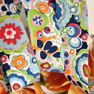 May include: A colorful fabric ribbon with a repeating pattern of flowers, leaves, and circles in shades of blue, green, pink, red, orange, and white.