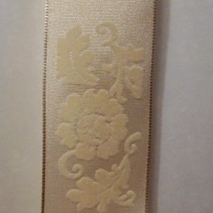 May include: A close-up of a white satin ribbon with a raised floral design. The ribbon has a subtle sheen and a delicate texture.