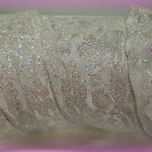Op de afbeelding: Wit kantlint met iriserende glitter. Het lint heeft een delicaat, ingewikkeld patroon en is perfect om een ​​toets van glitter toe te voegen aan elk knutselproject.